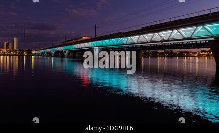 Beleuchtete Eisenbahnbrücke reflektiert in Tempe Town Lake in der Abenddämmerung in Tempe, Arizona, mit farbenfroher Beleuchtung und ruhigem Wasser. Stockfoto