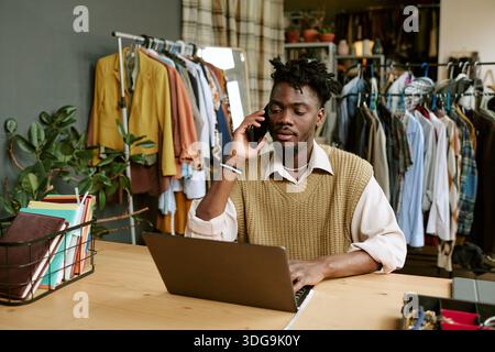 Junger Erwachsener Schwarzer Mann, Der Den Bestand Im Second Hand Clothing Store Aus Der Ferne Verwaltet Stockfoto