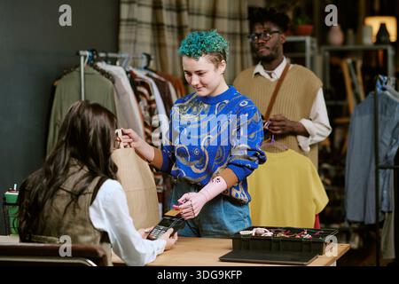 Junge kaukasische Frau mit Armprothese, die Kleidung im Second Hand Store kauft Stockfoto
