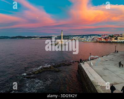 Blick aus der Vogelperspektive auf den Leuchtturm, der im Hafen bewacht wird, dessen Stein im Kontrast zum lebhaften Sonnenuntergang steht, Chania, Chania, Griechenland. Stockfoto