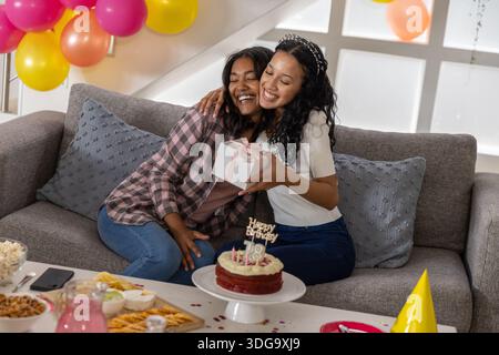 Die Mutter und die Tochter im Teenageralter tauschten eine Geschenkbox aus, während sie im Zimmer mit Kuchen auf dem Sofa saßen Stockfoto