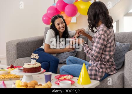 Verschiedene Eltern und Teenager-Tochter teilen sich Geburtstagskuchen auf dem Sofa im Wohnzimmer Stockfoto