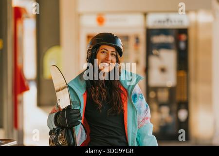 Lächelnde Frau, die Snowboard hält und Winterkleidung trägt, bereit für Schneesport Stockfoto