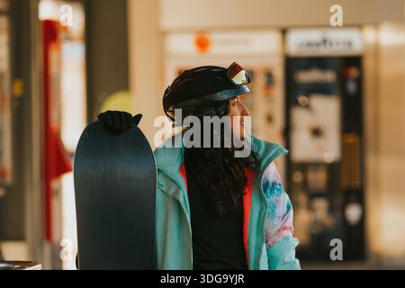 Eine junge Frau, die Snowboard hält und Winterkleidung trägt und mit Vorfreude nach vorne blickt Stockfoto