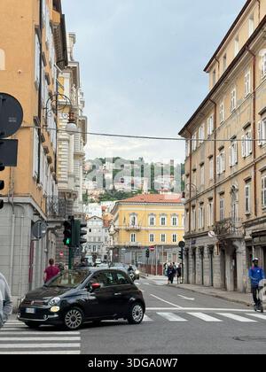 Panoramablick auf die Straße in Triest, Italien, mit einem klassischen Fiat 500, der durch eine lebhafte Kreuzung fährt Stockfoto