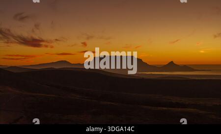Aus der Vogelperspektive auf den berühmten Tafelberg, der sich vor dem feurigen Sonnenuntergang mit langen Schatten über die hügelige Landschaft Kapstadt, Western, erstreckt Stockfoto
