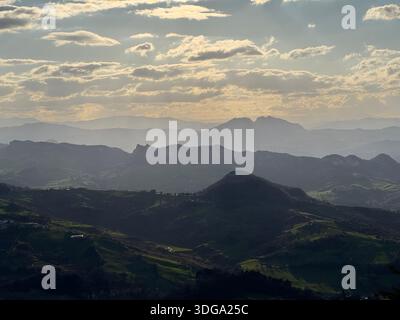 Geschichtete Hügel und nebelige Berge unter einem leuchtenden Himmel in der Landschaft von San Marino Stockfoto