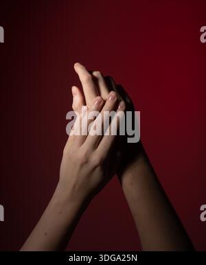 Hände mit Naturnägeln. Gepflegte glänzende Maniküre auf rotem Hintergrund zeigt Sorgfalt, Schönheit, Wellness und Eleganz. Die menschliche Geste drückt Harmonie und aus Stockfoto