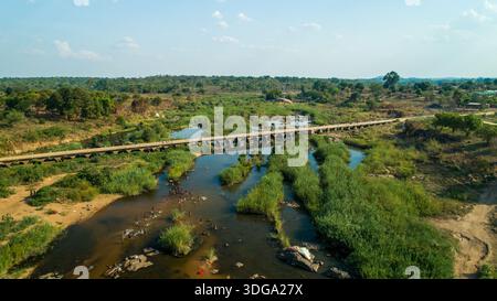 Aus der Vogelperspektive einer Brücke, die den pulsierenden Fluss überspannt, der durch die grüne Landschaft führt, ein starker Kontrast zwischen künstlicher Struktur und der rauen Natur Stockfoto