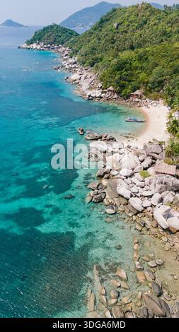 Aus der Vogelperspektive auf ein türkisfarbenes Meer, das sanft die zerklüftete Küste küsst, wo grüne Hügel auf den unberührten Sand von Ko Tao, Surat Thani, Thailand treffen. Stockfoto