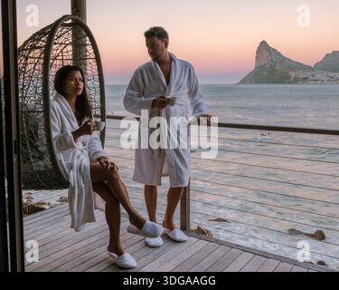 Paare genießen einen ruhigen Abend auf einer Holzterrasse mit Blick auf das Meer in Kapstadt am Morgen bei einem Kaffee Stockfoto