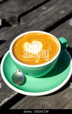Eine Tasse Kaffee mit herzförmiger Latte Art, serviert in grüner Keramikschale und Untertasse Stockfoto