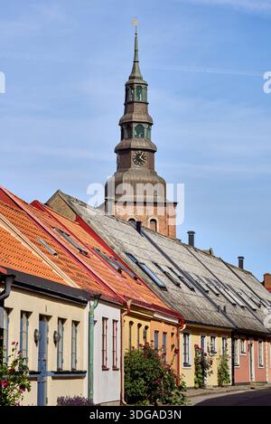 Farbenfrohe historische Häuser mit der Kirche oder dem Glockenturm der Kathedrale, die über den Dächern des Dorfes thront, an einem sonnigen Tag in Ystad, Schweden Stockfoto