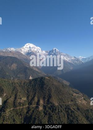 Aus der Vogelperspektive schneebedeckte Gipfel, die den Himmel durchdringen und Schatten auf den grünen Hängen darunter werfen, Annapurna, Nepal. Stockfoto