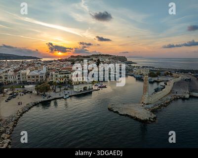 Aus der Vogelperspektive auf den venezianischen Hafen bei Sonnenuntergang, wo der alte Leuchtturm einen langen Schatten über das ruhige Wasser wirft, Rethimno, Rethymno, Griechenland. Stockfoto