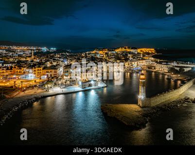 Aus der Vogelperspektive auf den beleuchteten venezianischen Hafen und Leuchtturm, der sich im dunklen Wasser spiegelt, mit der Festung Fortezza auf dem Hügel, Rethimno, Re Stockfoto