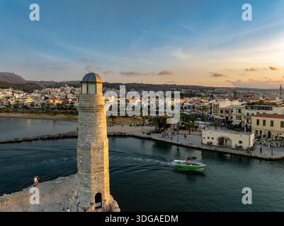Blick aus der Vogelperspektive auf den alten Leuchtturm, während ein lebhaftes grünes Boot durch das Hafenwasser gleitet, umgeben von der historischen Architektur von Re Stockfoto