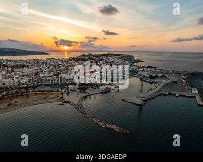 Blick aus der Vogelperspektive auf den venezianischen Hafen, umgeben vom goldenen Sonnenuntergang und dem alten Leuchtturm, mit der Silhouette der Festung Fortezza am Horizont, R Stockfoto