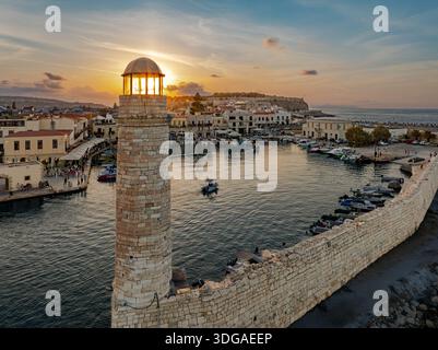 Aus der Vogelperspektive auf den sonnengeküssten Leuchtturm, der über dem ruhigen Hafen mit Booten wacht, eingerahmt von den alten venezianischen Mauern Rethimno, Re Stockfoto