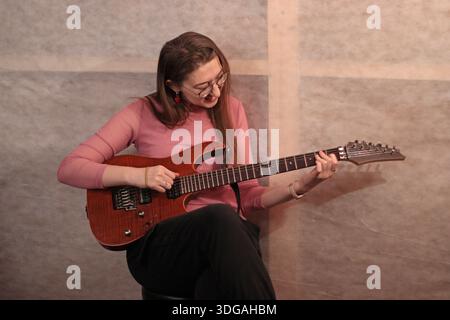 Die junge Frau sitzt in einem Tonstudio und spielt Gitarre Stockfoto