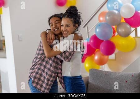 Verschiedene Mutter und Teenager-Tochter umarmen sich liebevoll im Zimmer mit Ballons, die an der Treppe befestigt sind Stockfoto
