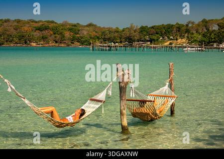 Thailand, Ko Kood, Westküste, Ao Bang Bao Strand, Besucher entspannen sich in Hängematten über kristallklarem Meer Stockfoto