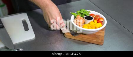 Banner des nicht erkennbaren Küchenchefs, der eine Gabel neben eine frische Poke-Schüssel mit Lachs in der Restaurantküche platziert Stockfoto