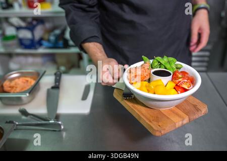 Nicht wiedererkennbarer Koch mit Schürze, der frische bunte Poke-Schüssel mit Lachs in der Restaurantküche zeigt Stockfoto