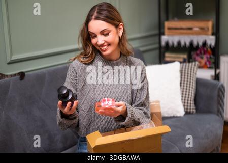 Eine fröhliche Frau, die sich Parfüms ansah, die sie online kaufte und im Paket geliefert wurde. Stockfoto