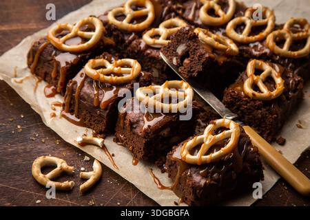 Schokoladen-Brownies mit Nüssen, gesalzenem Karamell und Brezeln, selektiver Fokus, hölzerner Hintergrund Stockfoto