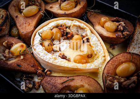Im Ofen gebackener Camembert-Käse mit karamelisierten glasierten Birnen, Walnüssen und Trauben sowie Baguette auf rustikalem Metallteller Stockfoto