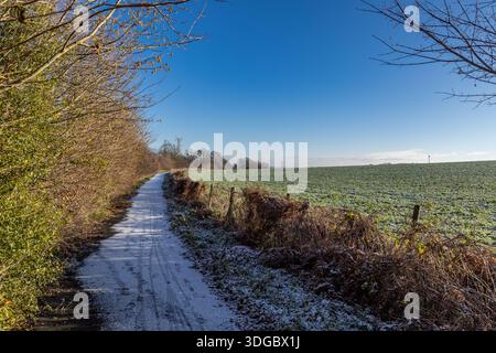 Ein schneebedeckter Pfad, der an einem sonnigen Wintertag entlang von Ackerland im ländlichen Sussex verläuft Stockfoto
