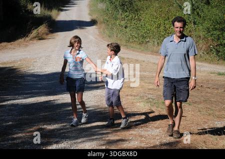 Ein Mann spaziert mit zwei Kindern auf einem Landweg und zeigt das Familienleben, die Aktivitäten im Freien und die Zweisamkeit bei einem Spaziergang auf dem Land. Stockfoto