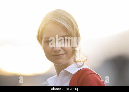 Ernst aussehende junge Frau in weißer Bluse und roter Strickjacke, im Hinterlicht, Stuttgart, Baden-Württemberg, Deutschland Stockfoto