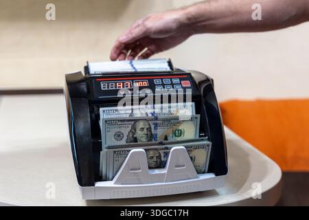 Wir zählen US-Dollar mit dem elektronischen Geldzähler. Nahaufnahme einer Hand mit einer digitalen Geldzählmaschine, um Stapel von US-Dollar zu verarbeiten Stockfoto