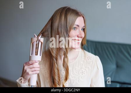 Junge Frau mit gesundem Haar mit Stylinggerät zu Hause, das moderne Schönheitsroutine repräsentiert Stockfoto