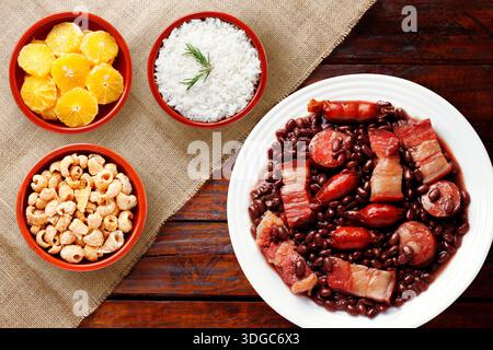 Traditionelle brasilianische Feijoada serviert auf einem weißen Teller mit schwarzen Bohnen, Wurst, Speck und Schweinefleisch, begleitet von weißem Reis, in Scheiben geschnittenem ​​oranges und po Stockfoto