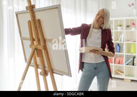 Junge Frau, die auf Leinwand malt und eine Palette hält Stockfoto