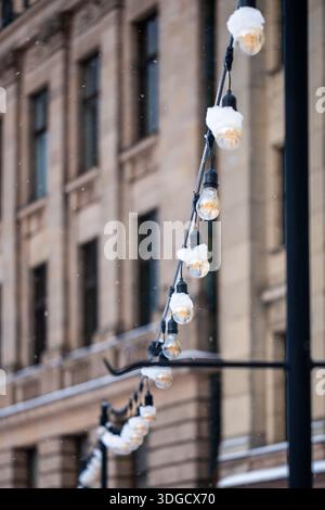 Schneebedeckte Lichterketten beleuchten eine winterliche Straßenszene, die vor dem Hintergrund historischer Gebäude ein warmes Leuchten ausstrahlen und das gemütliche Ambiente unterstreichen Stockfoto