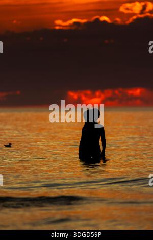 Silhouette einer Person, die während des intensiven roten Sonnenuntergangs über der Ostsee in Łeba, Polen, im Meerwasser steht. Stockfoto
