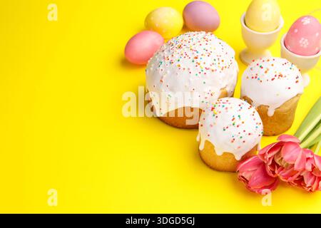 Köstliche Osterkuchen, Eier und Tulpen auf gelbem Hintergrund. Leerzeichen für Text Stockfoto