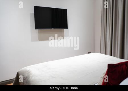 Moderne Hotelzimmer mit hübsch gefertigtem Bett, wandmontiertem Fernseher und minimalistischem Design in neutralen Farben. Ideal für Reiseunterkunftskonzepte Stockfoto