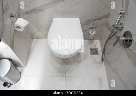 Modernes Hotelbad mit wandmontierter Toilette, Bidet-Dusche, Toilettenbürste und Edelstahlmüll auf Marmorboden Stockfoto