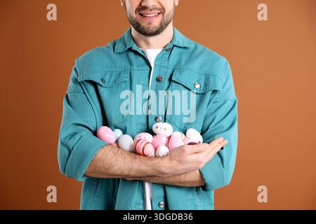 Osterfeier. Lächelnder Mann, der bemalte Eier auf braunem Hintergrund hält, Nahaufnahme Stockfoto