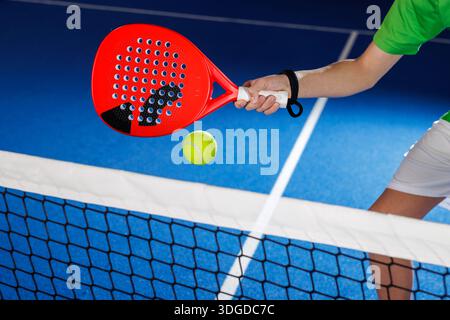 Nahaufnahme eines Padel-Spielers, der über dem Netz auf dem blauen Hallenplatz für Trainingswettbewerbe und Sportmarketing spielt Stockfoto