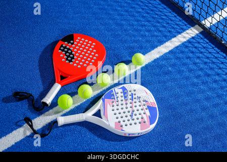 Zwei Padel-Schläger und mehrere Bälle auf blauem Hallenplatz per Netz bereit für Übungsausrüstung Konzept mit Kopierraum Stockfoto