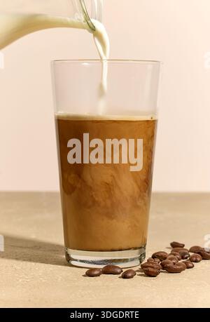 Milchgießen in Glas Kaffee auf beigem Hintergrund Stockfoto