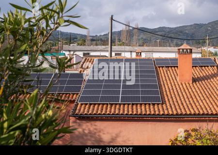 Solarpaneele sind auf einem Terrakotta-Dach installiert, umgeben von Grün und fernen Hügeln, die nachhaltige Energielösungen in einem Wohnbereich hervorheben Stockfoto