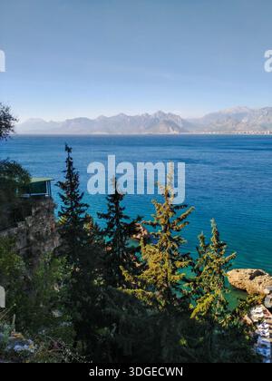 Kiefern wachsen an felsigen Hängen mit Blick auf das tiefblaue Meer und die fernen Berge. Stockfoto