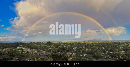 Ein spektakulärer Panoramablick auf einen kompletten doppelten Regenbogen, der sich über einen grünen Vorort in Melbourne, Australien, erstreckt. Stockfoto